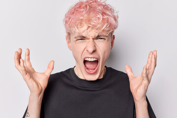 People negative emotions concept. Studio photo of young angry European boy with pink hair crying standing in centre isolated on white background wearing black casual t shirt keeping hands raised