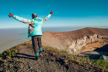 A hiker at the summit of Mount Ol Doinyo Lengai with the volcanic crater - the ash pit in...