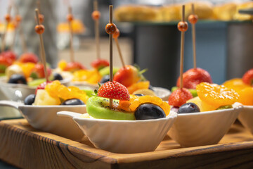 Fruit salad in a white bowl on a wooden tray prepared for a buffet table. Close-up