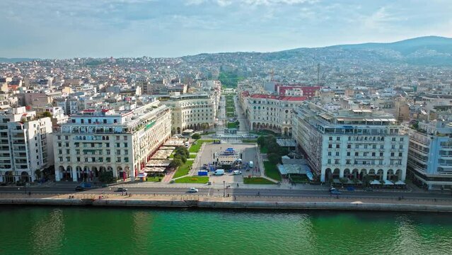 Aerial view of Vast, waterfront public square Aristotelous in Thessaloniki. View from above of ample, paved square surrounded by Neoclassical buildings, with a green park in the middle.
