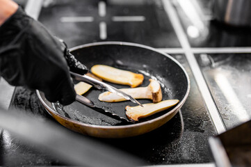 Professional chef cooking mushroom in frying pan on stove in restaurant kitchen
