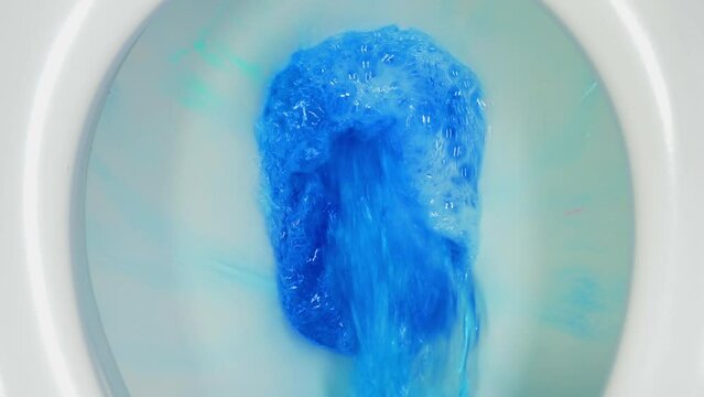 Closeup overhead shot of a white toilet flushing with cleansing blue color water, which acts as a limescale inhibitor and also adds fragrance.