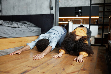 Image of african american young couple doing downward facing dog posture doing yoga ta home, dressed in casual clothes, relaxing after stressful week, exercising in bedroom on floor