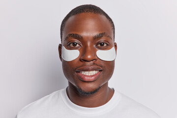 Headshot of dark skinned adult African man applies beauty patches under eyes to reduce wrinkles...