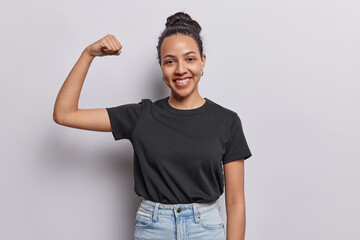 Horizontal shot of active cheerful Latin woman shows biceps keeps arm raised happy to achieve nice...