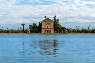 Photo of the Menara Gardens in the city of Marrakech. Photo of the lake with the house at the end of the lake. The house reflected in the lake. Cloudy day.