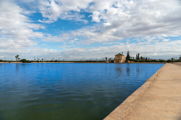 Photo of the Menara Gardens in the city of Marrakech. Photo of the lake with the house at the end of the lake. The house reflected in the lake. Cloudy day.