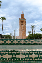 Photo of the tower of the Koutoubia mosque. Park with a fountain. Cloudy day.