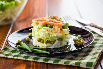 Layered salad of cabbage and other vegetables with pieces of red fish in a plate.