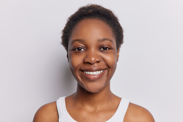 Portrait of lovely dark skinned pretty teenage girl with short curly hair smiles toothly has...