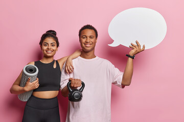 Indoor shot of Iranian woman and African man carry foam roller and weight show blank communication bubble for your text isolated over pink background lead healthy lifestyle. People and sport concept - obrazy, fototapety, plakaty