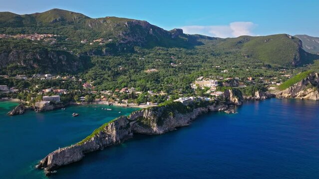 Aerial view of tourist resorts and luxury hotels in Palaiokastritsa, Corfu. Agia Triada Beach with turquoise water, sand mixed with pebbles around the shore, and bottom covered with flat rocks.