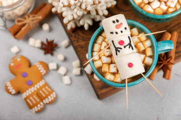 Fototapeta premium Hot drink with marshmallows and candy cane in cup on texture table.Cozy seasonal holidays.Hot cocoa with gingerbread Christmas cookies.Hot chocolate with marshmallow and spices.Copy space.