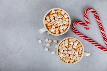 Obraz na płótnie Canvas Hot drink with marshmallows and candy cane in cup on texture table.Cozy seasonal holidays.Hot cocoa with gingerbread Christmas cookies.Hot chocolate with marshmallow and spices.Copy space.