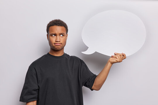 Serious discontent dark skinned man holding empty bubble speech cloud demonstrates his thoughts dressed in casual black t shirt being dissatisfied with something isolated over white background