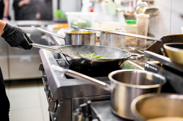 Professional chef cooking asparagus in frying pan on stove in restaurant kitchen