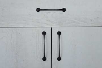 Cabinet doors made of laminated chipboard with abstraction in the form of concrete in macro. Close-up of evenly adjusted white structure chest of drawers with black vintage handles.