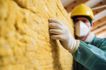 Male construction worker with protective mask installing mineral wool filling used as isolation material in walls