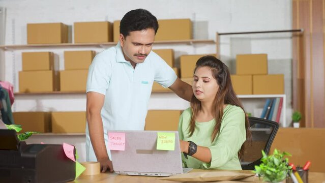 Indian coworkers or couples discussing from laptop while working together at ecommerce warehouse - concept of teamwork, collaboration and business communication