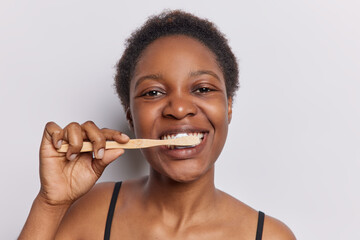 Photo of young dark skinned young woman with curly hair brushes teeth with toothbrush undergoes...