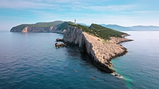 Aerial view of Phare de Akrotiri Lefkada Lighthouse in Cape Doukato. View from above of a white tower on a rocky cliff by the edge of the coast in Lefkada surrounded by emerald-blue waters.