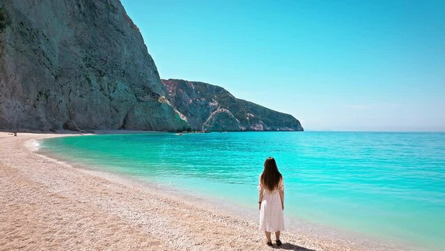 Tourist woman enjoying summer vacation at Porto Katsiki beach with turquoise water by cliffs. Aerial view of a young girl relaxing on Ionian island of Lefkada, Greece with crystal clear blue waters.