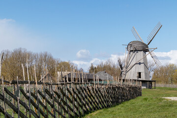 Wooden windmill with a wooden fence on a background of grass and blue sky