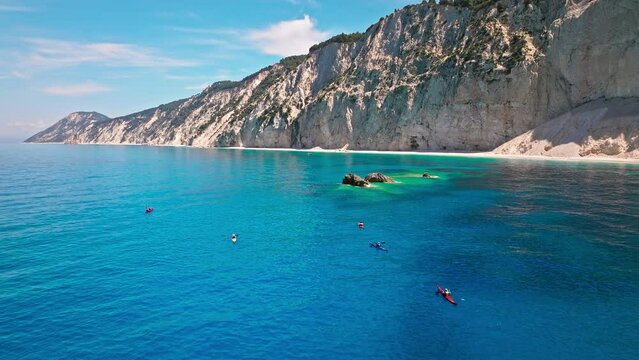 Kayaking Holidays on Porto Katsiki beach with turquoise water bordered by concave pale cliffs. Aerial view of tourists kayaking on crystal clear blue waters on the Ionian island of Lefkada, Greece.