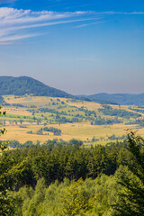 Fototapeta premium Beautiful green and blue panorama of layers of mountains and trees and some fields seen from top of viewing tower at highest mountain in this area
