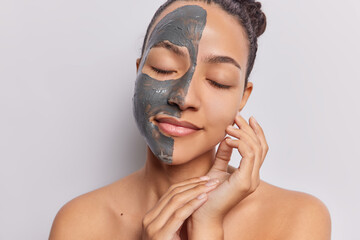 Portrait of young Latin woman applies facial clay mask for skin nourishment keeps eyes closed from...