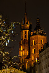Fototapeta premium The tower of St. Mary's Basilica in Krakow against the background of Christmas decorated trees. Night view of Krakow's Old Town.