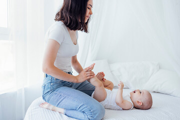 Pretty infant in a white bodysuit with his mom on a light background. Motherhood concept.