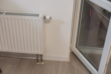 A steel panel heating radiator is placed under the windowsill on a white wall.