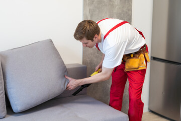 Rear View Of Young Male Worker Cleaning Sofa With Vacuum Cleaner