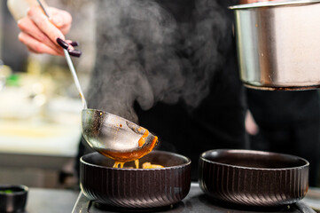 chef pouring tasty soup from pot into bowl on kitchen
