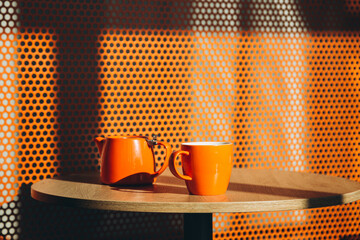 A cup of tea and a kettle in a minimalist orange cafe interior. Cozy cafe on a sunny morning. A...