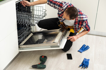 Repair of dishwashers. Repairman repairing dishwasher in kitchen 