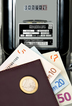 Brieftasche mit Euroscheinen und Euromünze vor Stromzähler