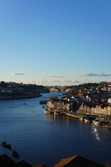 Obraz premium This image shows a row of cozy riverside homes in the Ribeira district of Porto, Portugal. The homes are built of stone and wood and have red-tiled roofs. They are located along the banks of the Douro