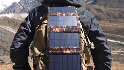 Portable folding solar panel is attached to tourist backpack in close up. Sun shines on panel charging traveler gadgets in absence electricity. Hiking in mountains or wilderness. Modern technologies - Powered by Adobe