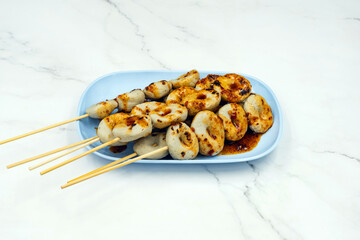 The delicious grilled fish meatballs and seasonings with spicy sauce on dish with marble background. Grilled meatballs Made from meat. Asian Street Food. Roasted meatballs with sauce on blue plate.