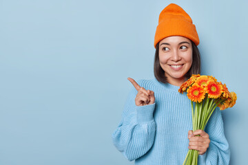 Beautiful young Asian woman with cheerful tender expression holds bouquet of orange daisy flowers...