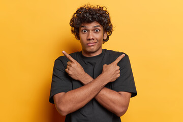 Studio shot of young confused Hindu male student standing in centre isolated on yellow background...