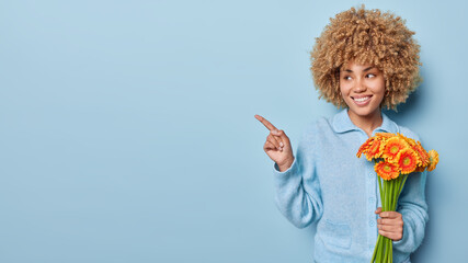 Horizontal shot of pretty curly haired young woman dressed in casual jumper holds bouquet of orange...