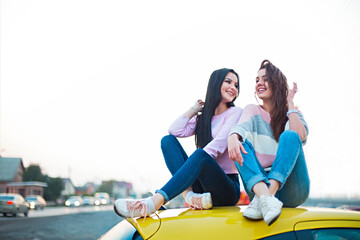 Best female friends cheering by car road trip at sunset. Happy people outdoor on vacation tour