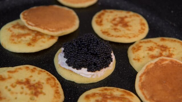 Blinis with black caviar and cream cheese, on a festive dish, mini pancakes, an elegant appetizer, High quality 4k footage
