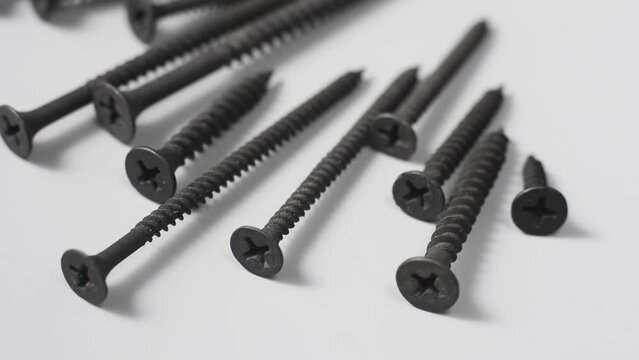 metal screws scattered on neutral gray background, black drywall screws phosphate coated to protect from rust used in building, industrial concept