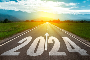 New year 2024 concept. Text of 2024 and arrow written in the middle of asphalt road on background of sunset and mountains.