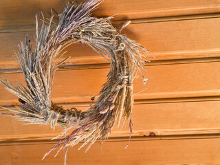 A wreath of dry grass hangs on a wooden wall.