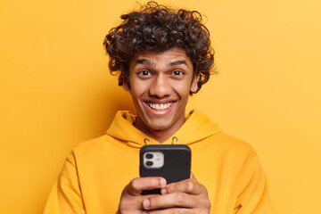 Positive Hindu man holds smart phone writing post using mobile device for communication smiles...